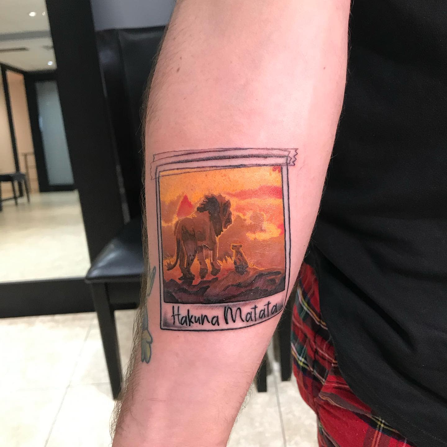 Polaroid-style tattoo of a lion and cub from Lion King on an arm with "Hakuna Matata" text below